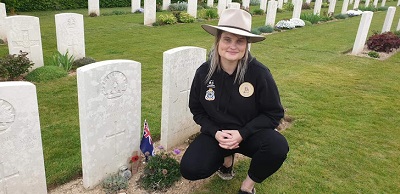 Mel Burnett kneeling at unknown soldier's grave where she has placed a flag and jar of sand