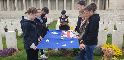 Students from the holding the Australian flag in a Commonwealth War Graves Commission cemetery as Elizabeth Perkins reads information