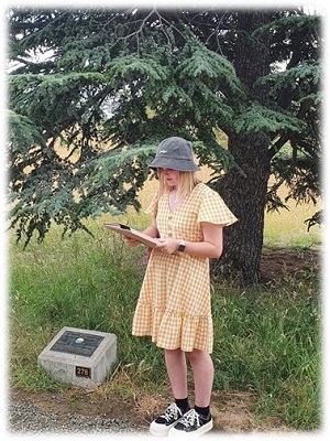 A young woman reading a report while standing near a plaque under a tree