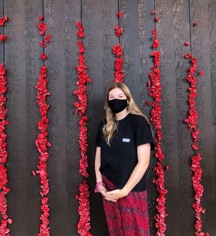 Zoe Rogers standing near a memorial wall containing soldiers' names and red poppies