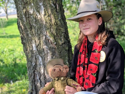 Nell Hentschel holding a teddy bear in military uniform with tree trunk as background