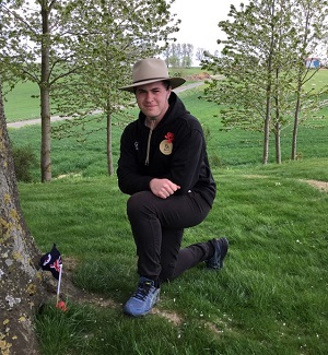 William Scott kneeling near a tree where a small Australian flag is planted in the ground