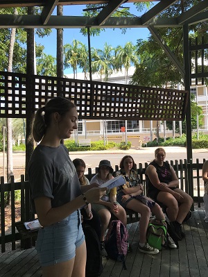 Chloe Britain reading research to a group of people. It is sunny outside and the people are under shade.