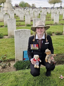 A young woman with two teddy bears, one dressed a nurse and the other dressed as a soldier, in a military cemetery